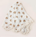 White baby blanket with brown bear patterns and white tassels on a beige background