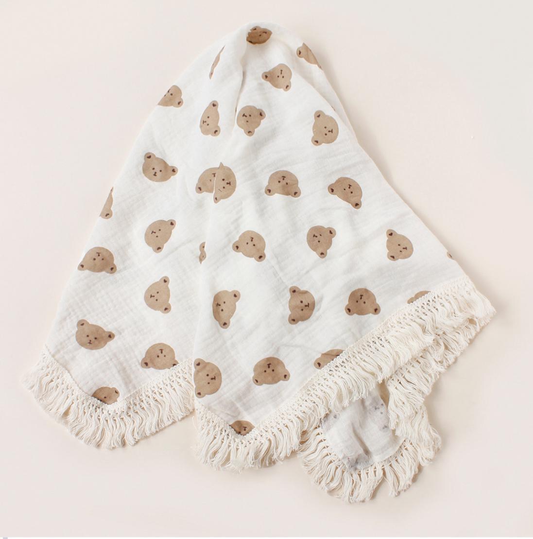 White baby blanket with brown bear patterns and white tassels on a beige background