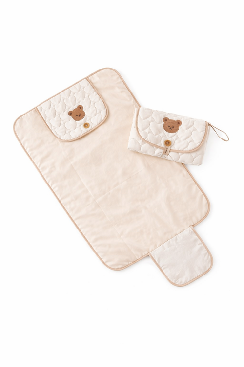 Beige quilted baby changing mat with bear face design on a white background