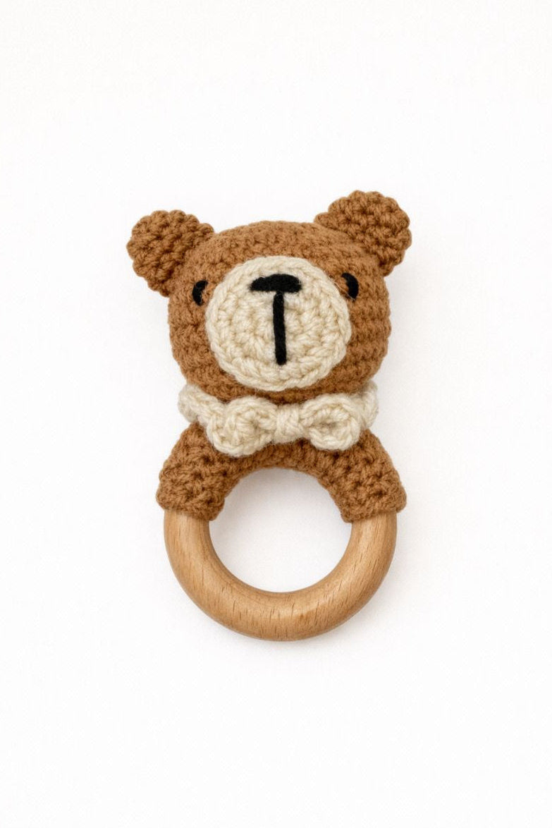 Crocheted teddy bear rattle with wooden ring on a white background