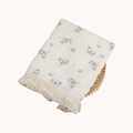 White blanket with green floral patterns and frayed edges on a white background