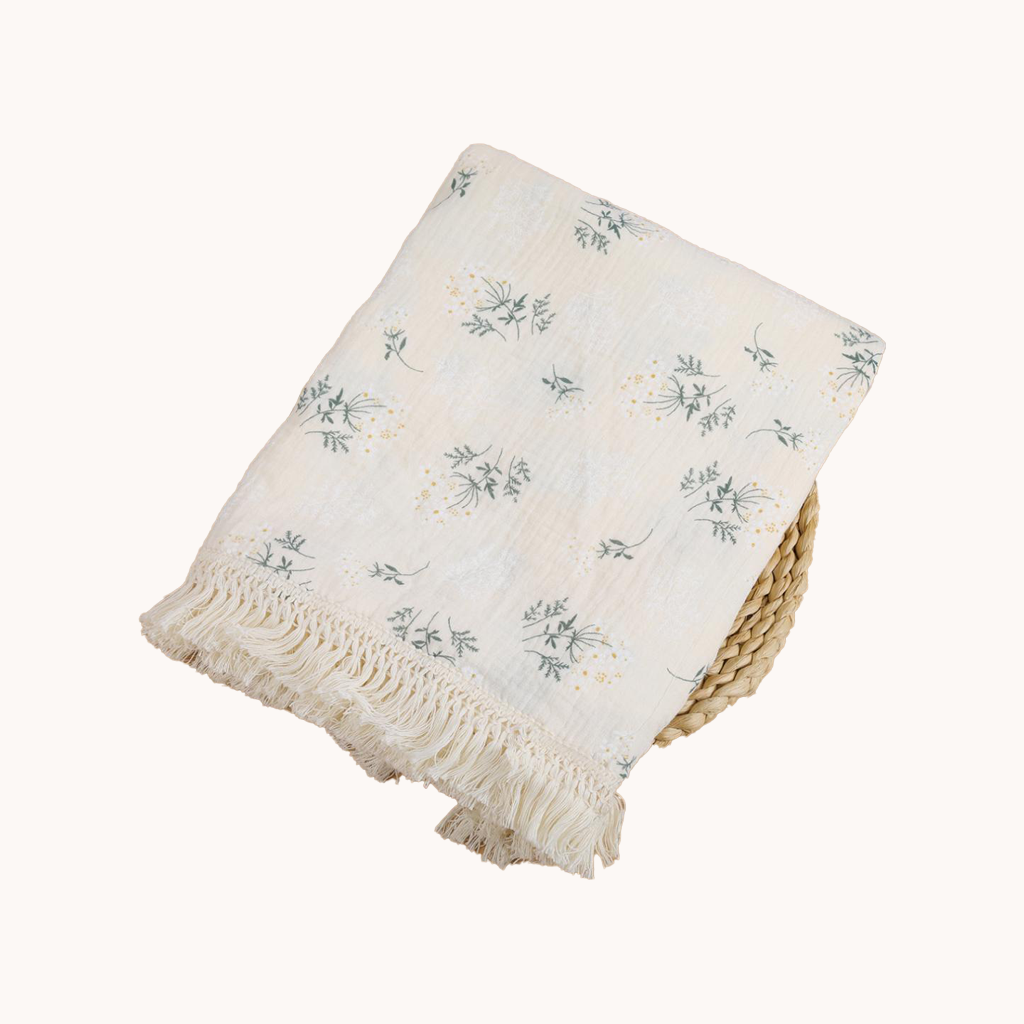 White blanket with green floral patterns and frayed edges on a white background